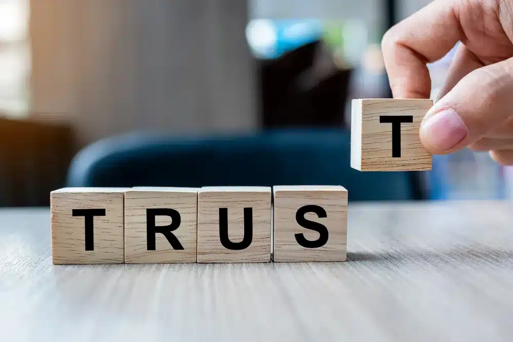 businessman-hand-holding-wooden-cube-block-with-trust-business-word-table-background